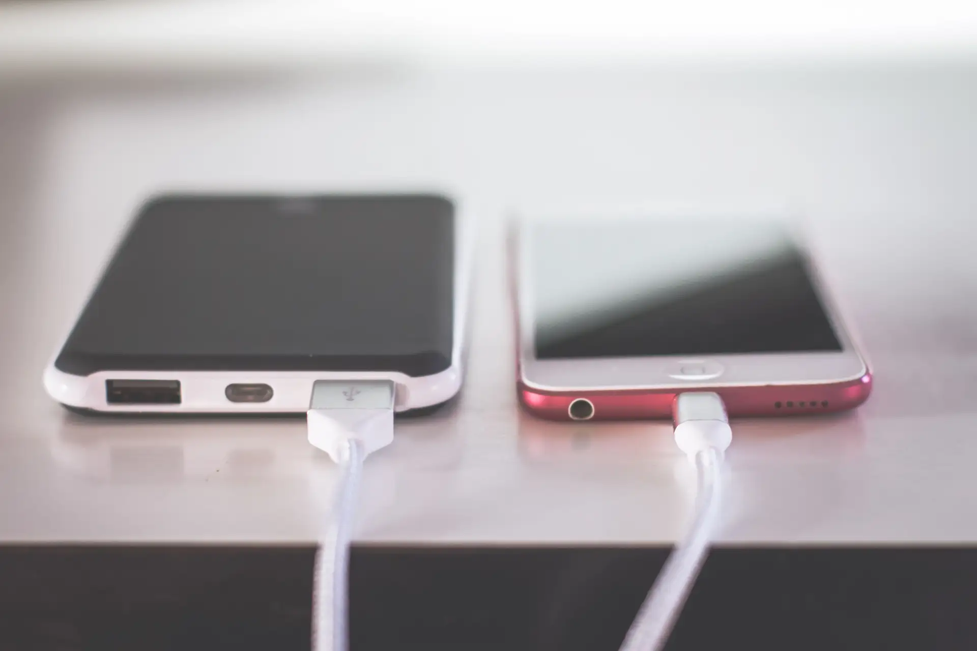 Smartphone branché à un câble de charge posé sur une table en bois, écran éteint